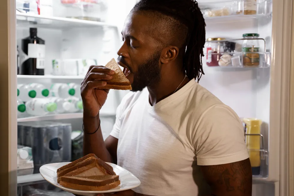 Hombre comiendo con la nevera abierta